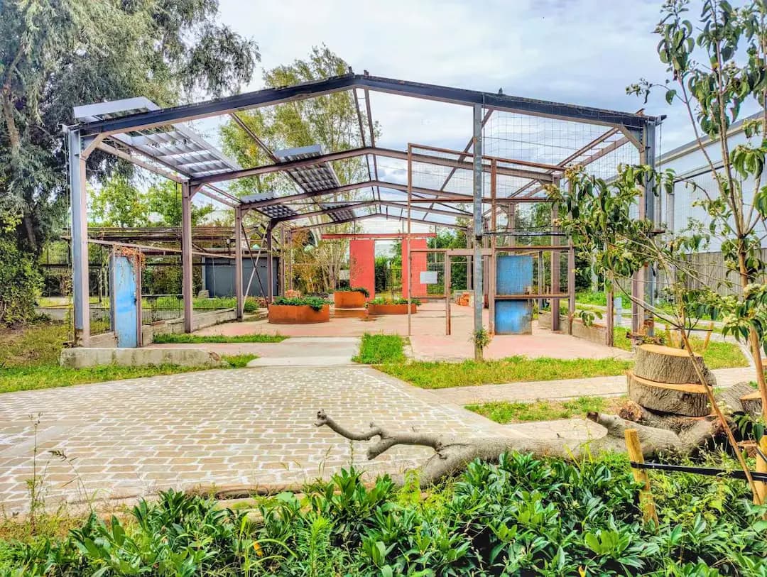 De open staalhal van de oude fabriek, gezien vanaf de fietswegel: een roestbruin staalskelet met planters eronder en een klinkerpad dat ernaartoe loopt
